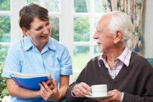 Older adults sharing a meal while a caregiver assists a resident in a bright community dining room.