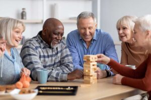 Older adults share a meal in a bright assisted living dining room while a caregiver offers gentle support.